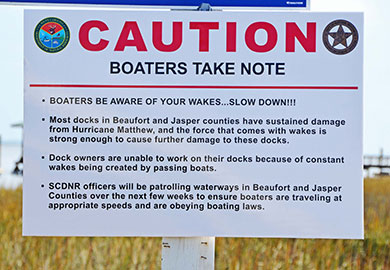 Warning signs ask boaters to control speeds and reduce wakes in damaged areas.