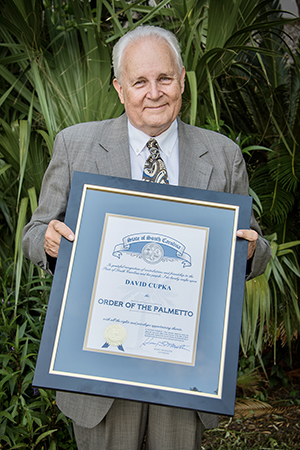 David Cupka smiling and holding a framed award with his name and ORDER OF THE PALMETTO on it.