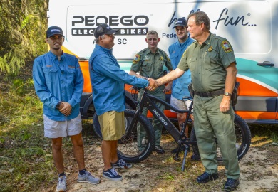 Major Gary Sullivan with the SCDNR shakes hands with Pedego of Aiken owner Coker Day during a day spent testing the new electric bicycle being donated to the agency. Also pictured are Pedego of Aiken Manager Shane LeDonne (far left), SCDNR Lance Corporal Jeff Day (center) and Pedego of Aiken Mechanic Ryan Blane. [SCDNR photo by David Lucas]