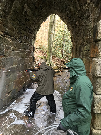 SCDNR Heritage Trust staff (from left) Brian Long and Abel Tobias use a pressure washer to remove graffiti from historic Poinsett Bridge at the heritage preserve in northern Greenville County. (SCDNR photo by Greg Lucas)