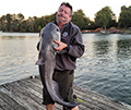 Man holding a catfish, length of the catfish is from his shoulders to past his knees