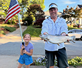 a man holding a Brown trout standing next to a girl holding the american flag