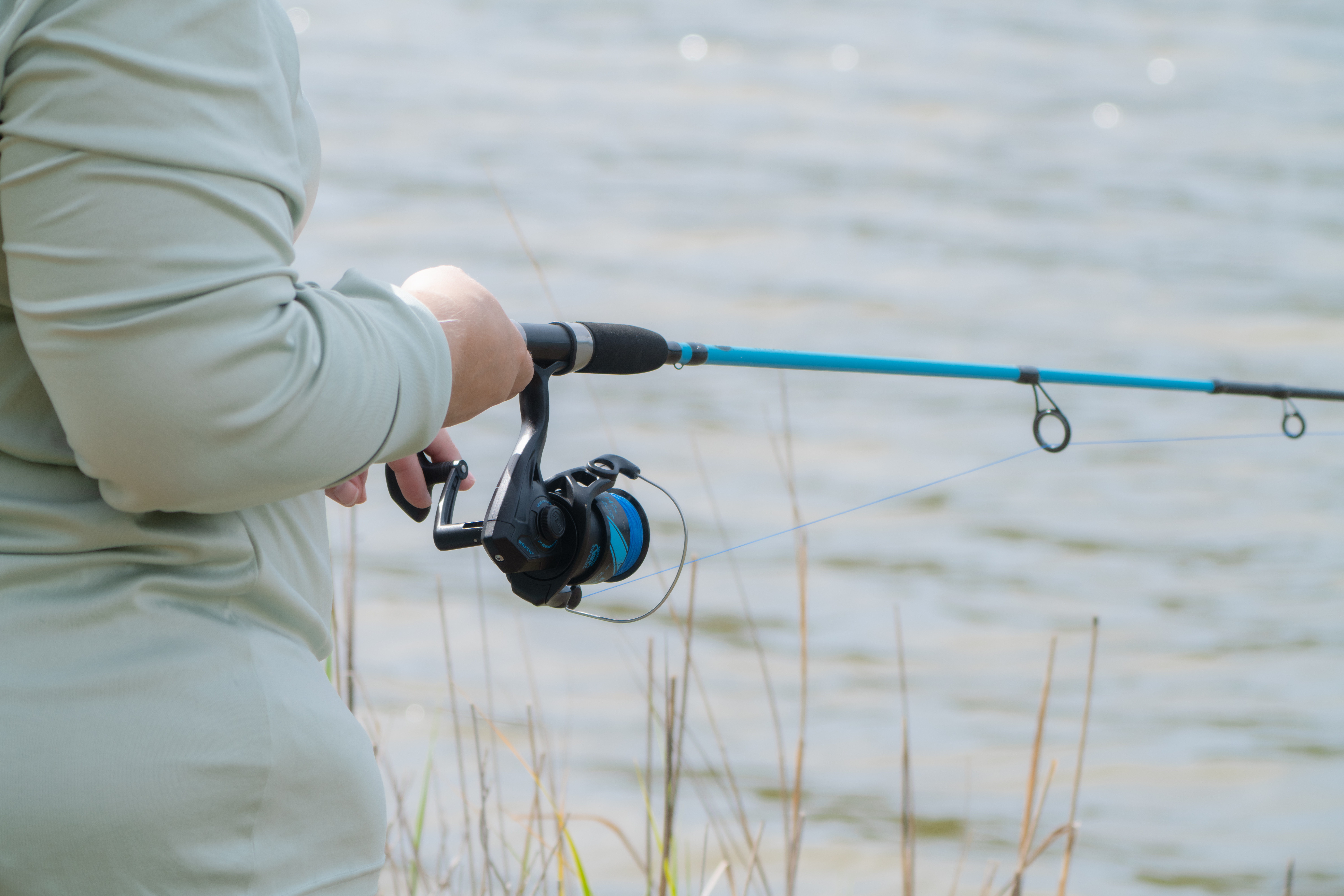 Someone holding a fishing rod with water in the background